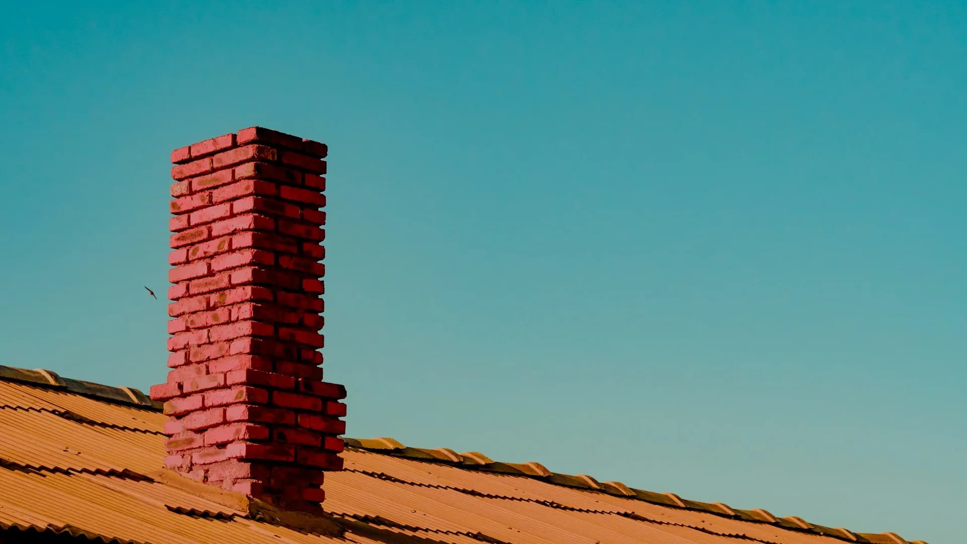 Brick chimney rising through a tile roof at sunset